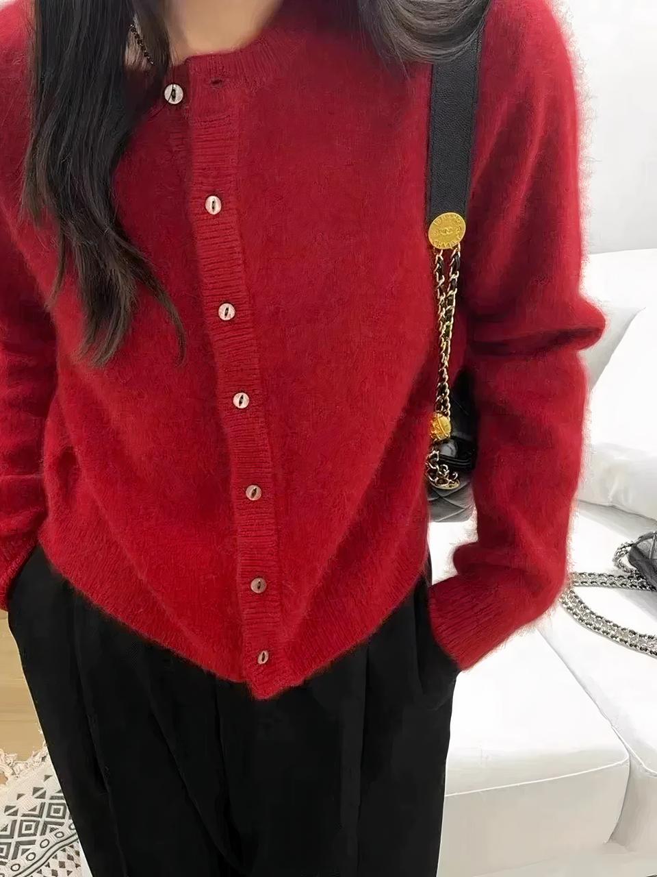 Photo représentant une femme debout les mains dans les poches de son pantalon noir dans un salon avec canapé blanc en cuir, parquet clair et tapis beige et portant un cardigan rouge à col rond en cachemire à boutonnage simple de huit petits boutons