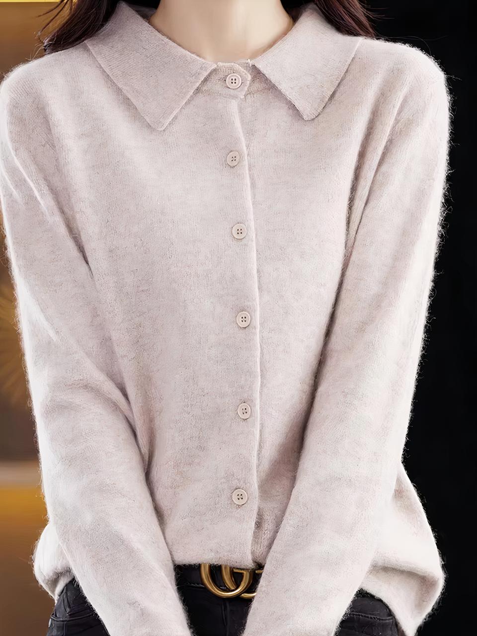 Photo d'une femme portant un cardihgan beige en cachemire à col polo fermé par boutonnage simple et manches longues sur un pantalon noir avec ceinture à boucle dorée, le fond est marron foncé