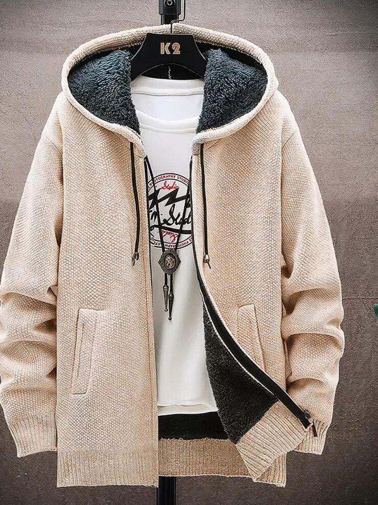 Photo d'un cardigan beige pour homme à capuche entièrement doublé polaire gris foncé avec fermeture par zip sur un teeshirt blanc imprimé noir et rouge , un collier long, sur un cintre marron foncé en bois, le tout sur fond blanc