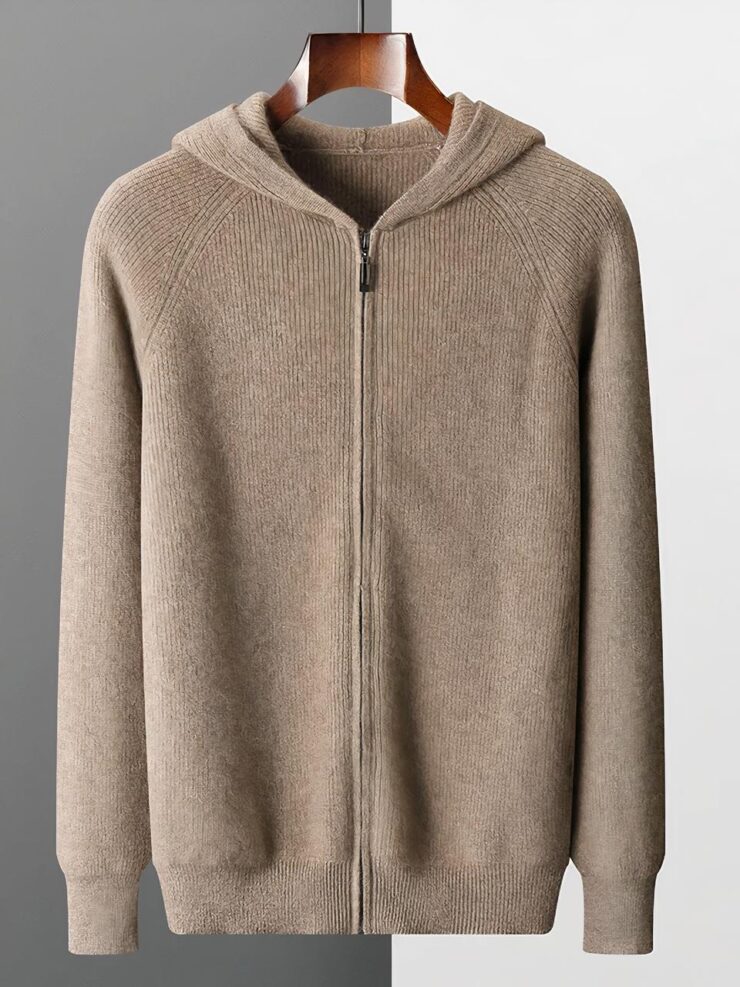 Photo d'un cardigan à capuche marron clair zippé en maille fine sur un cintre en bois marron, le tout sur un fond gris clair à droite et gris foncé à gauche