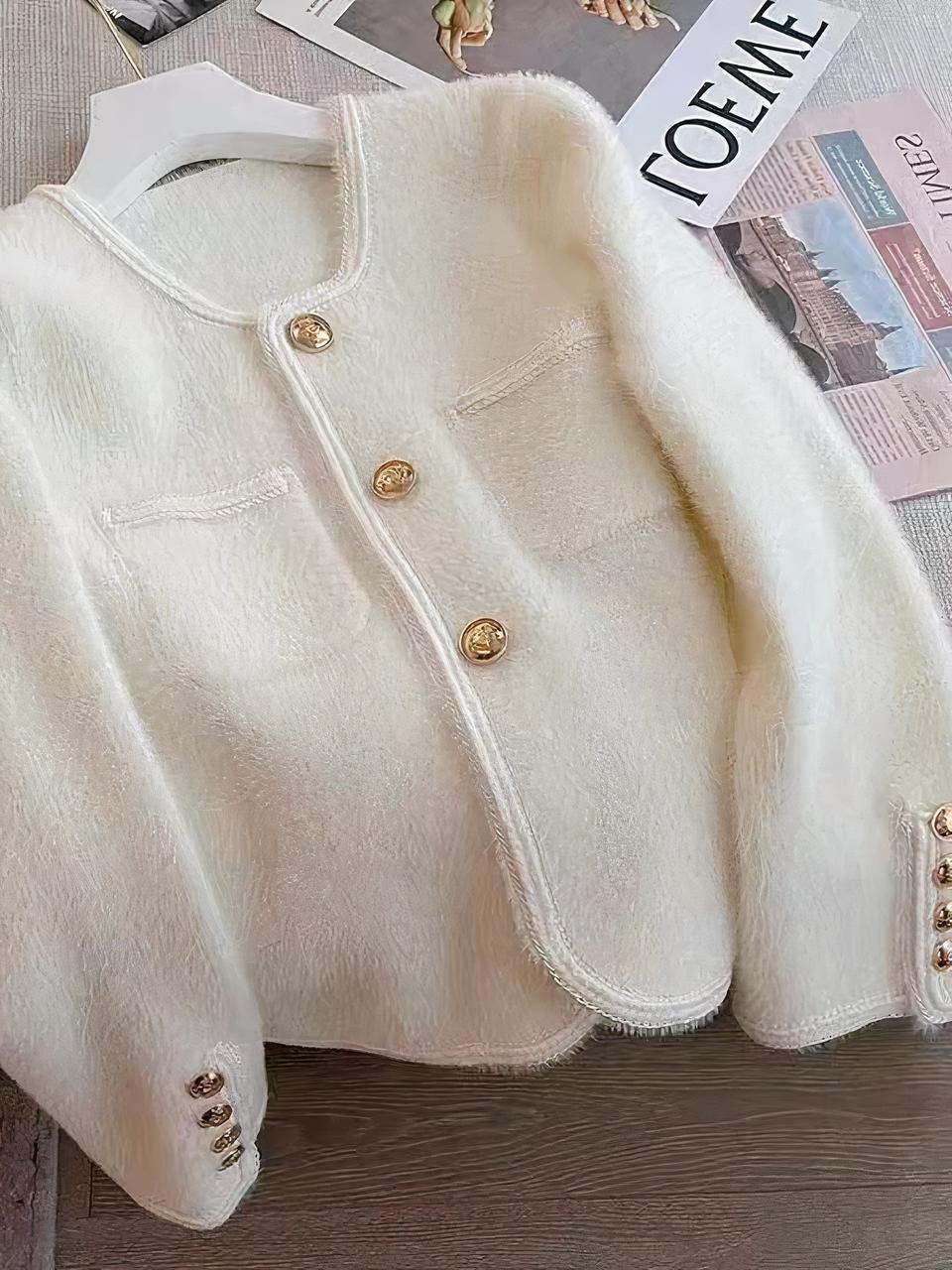 Cardigan blanc avec des boutons dorés sur un cintre.