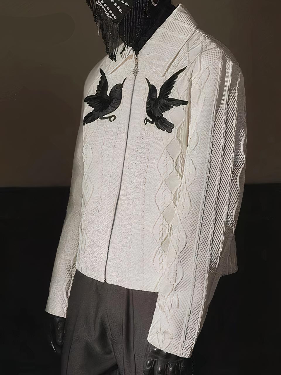 Un cardigan zippé blanc avec 2 oiseaux noirs et un motif jacquard blanc. Porté avec un pantalon noir