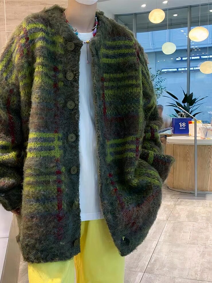 Un homme porte un pantalonjaune, un tee shirt blanc et une veste mi-longue rayée jaune, violet et vert