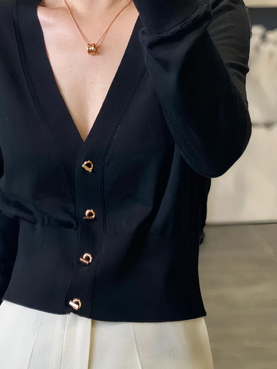 Photo d'une femme debout portant un cardigan noir fin col en V profond à quatre boutons mousquetons sur un pantalon en toile blanche, main droite dans sa poche