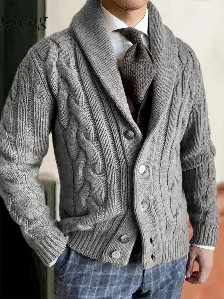 Un homme porte un gilet gris à torsades avec un col châle, une chemise blanche, une cravatte et un pantalon à carreaux