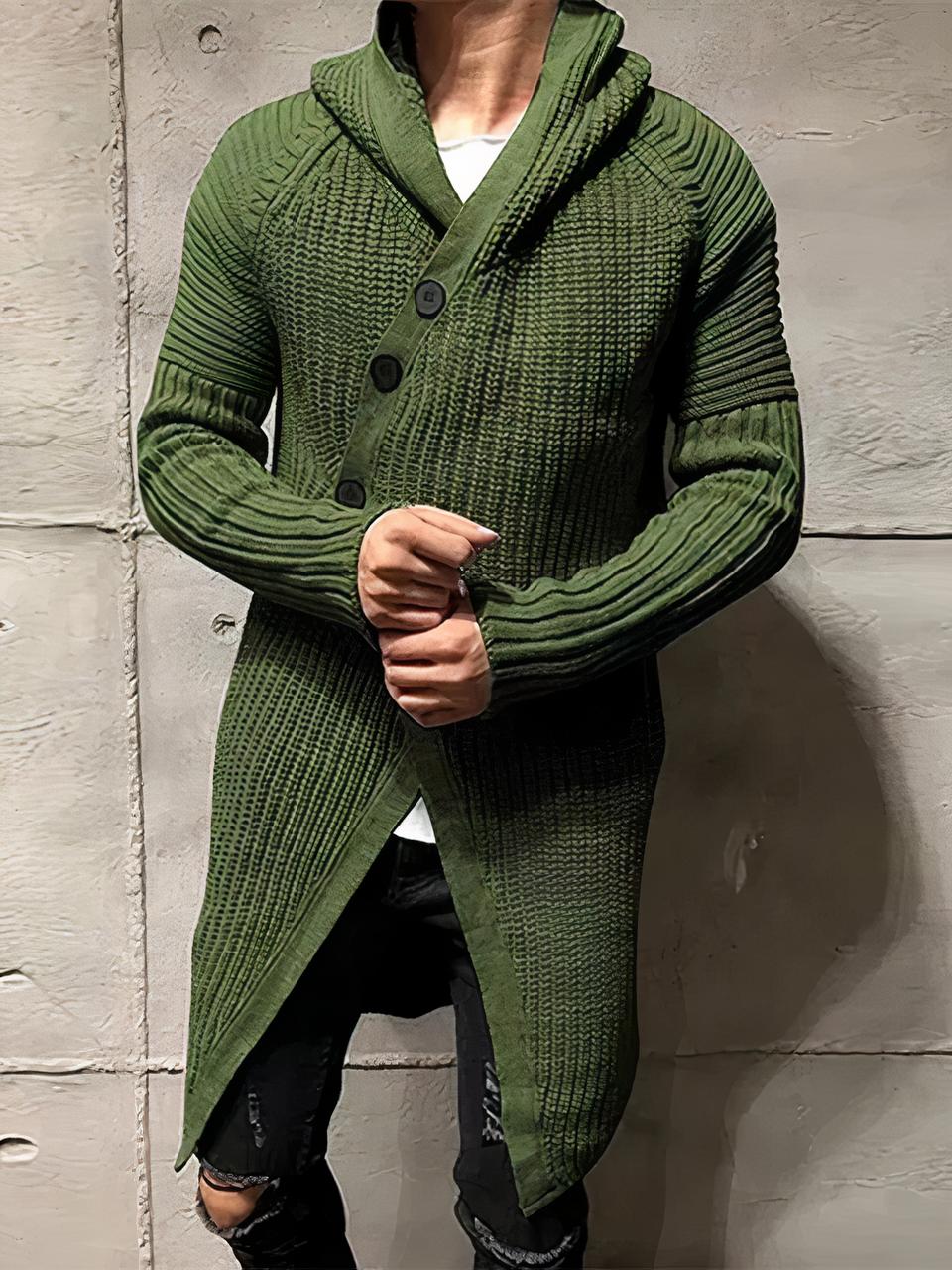 Cardigan long homme boutonnage asymétrique Photo d'un homme dos sur un mur de béton beige clair les mains posées sur le cardigan long et vert à boutonnage asymétrique et à capuche sur un pantalon skinny noir à trous et un teeshirt blanc