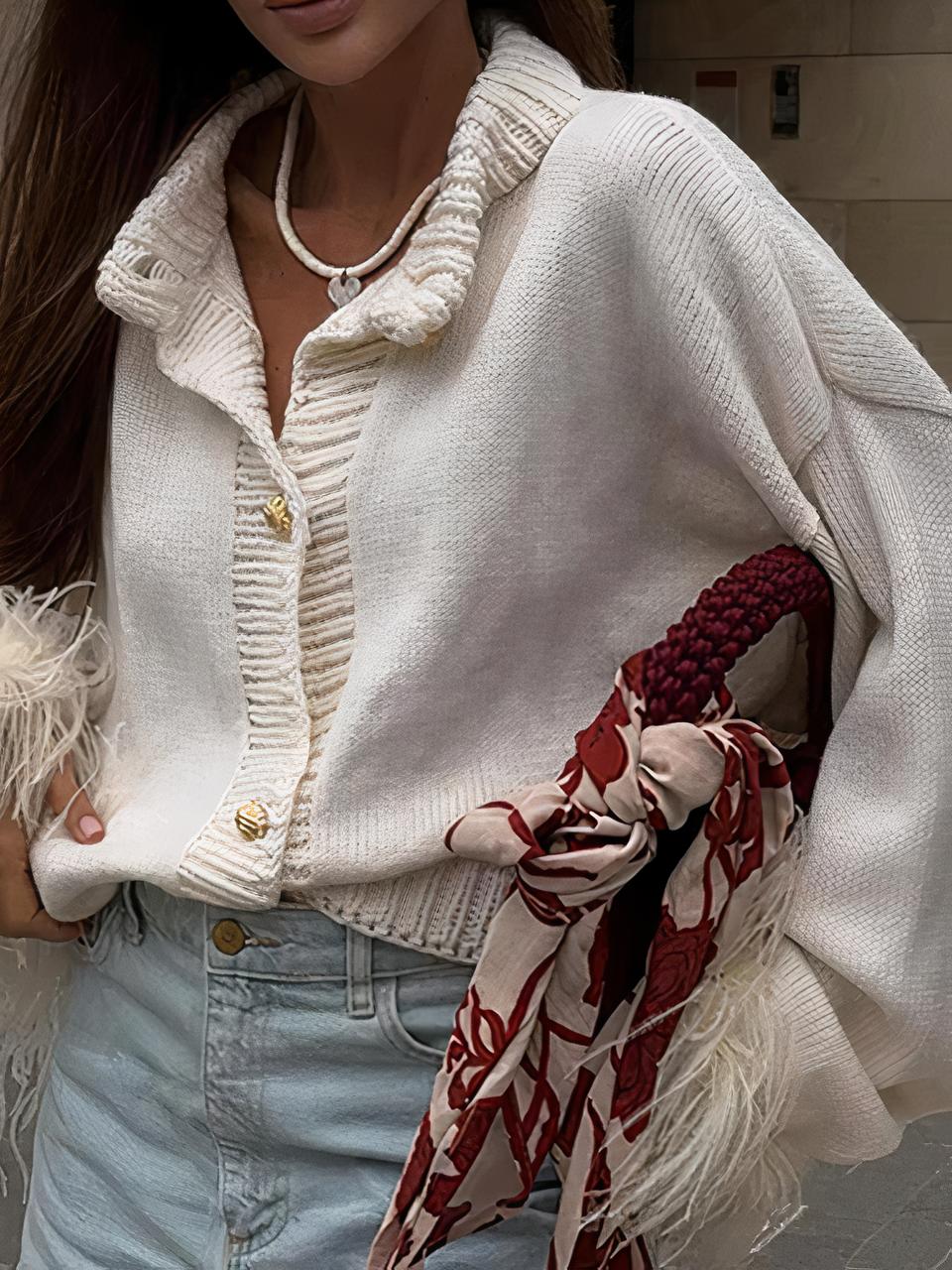 Photo d'une jeune femme portant un cardigan en maille blanche court à col rond épais ouvert et bout de manches ornés de plumes sur une jupe en jean bleu ciel, un sac à main bordeaux avec foulard assorti sur l'anse sous le bras gauche, le tout dans une rue
