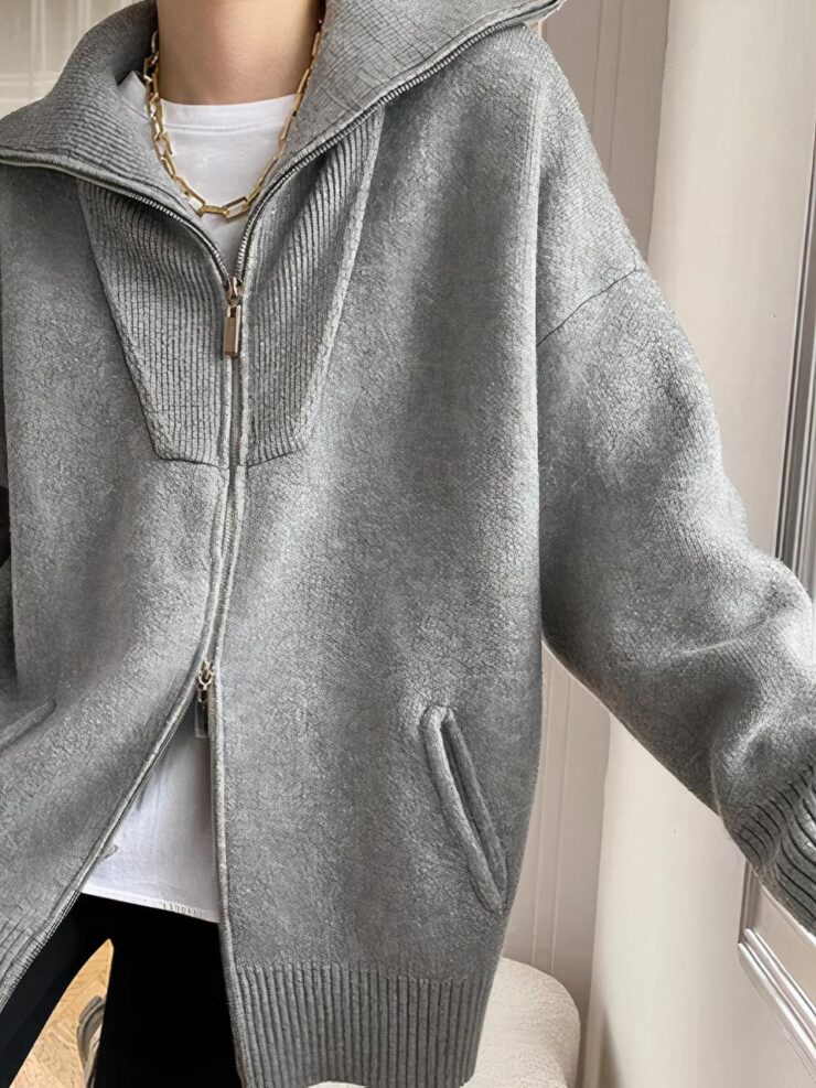 Cardigan gris long avec 2 fermetures éclair et des poches, porté par une femme en tee shirt blanc et un pantalon bleu