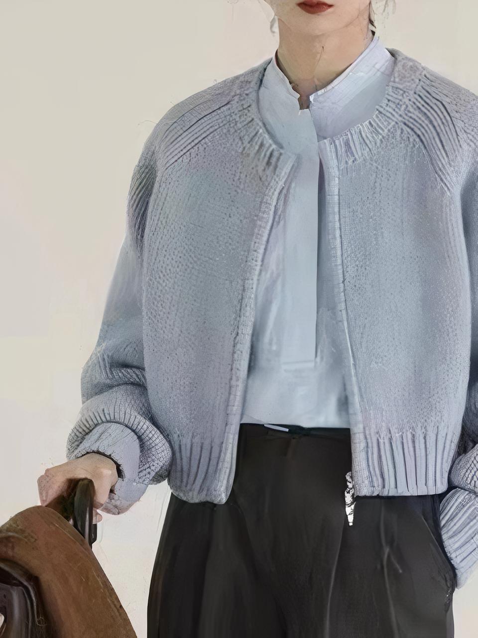 Une femme porte un chemisier bleu clair, un pantalon noir et un cardigan bleu ciel zippé. Une main dans la poche du pantalon