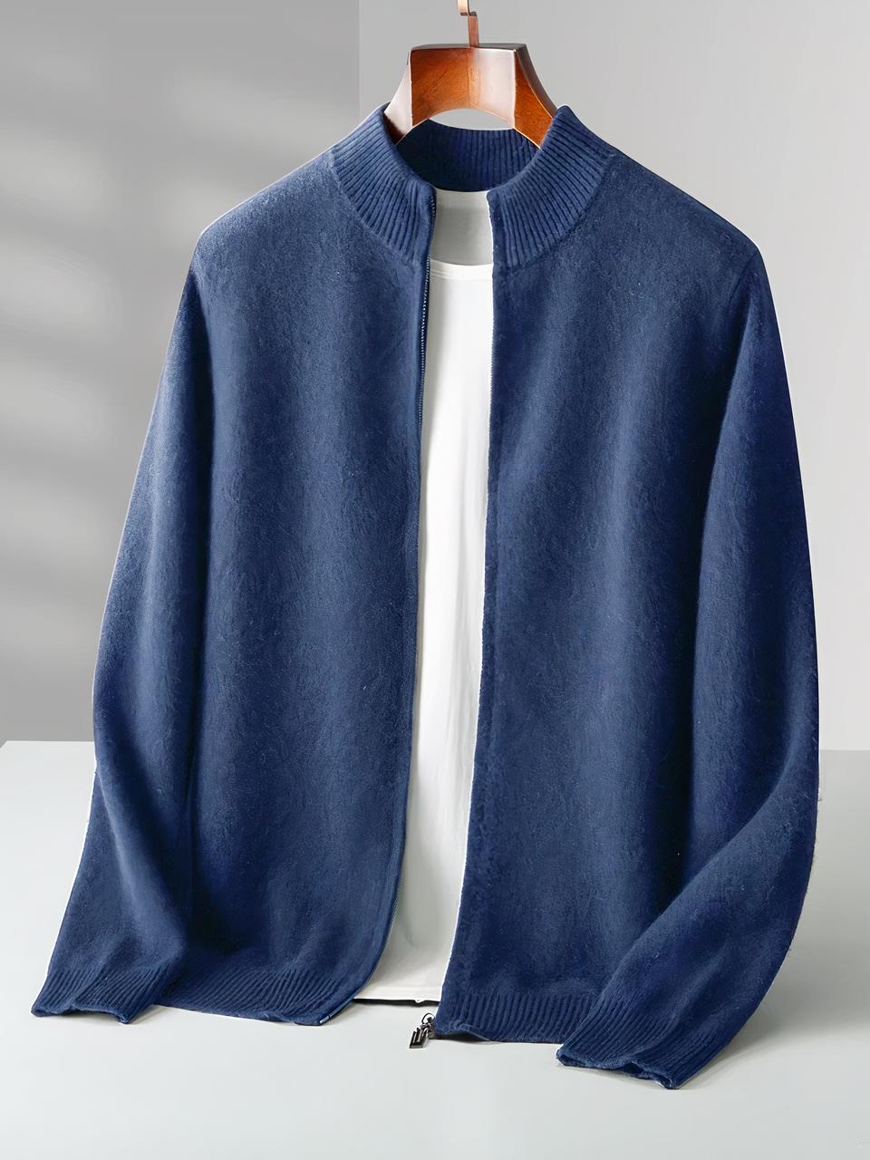 Cardigan zippé homme 100% laine Mérinos Photo d'un cardigan bleu zippé sur un cintre en bois avec un teeshirt blanc en dessous, il repose légèrement sur un bloc blanc avec un fond gris-blanc