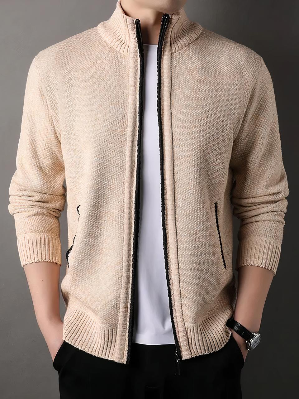 Cardigan zippé homme à fermetures noires Photo d'un homme debout portant un cardigan beige à fermetures éclairs noires poches et devant, et col montant, sur un teeshirt blanc et un pantalon noir, les mains dans les poches, le fond est marron clair à gauche et marron foncé à droite