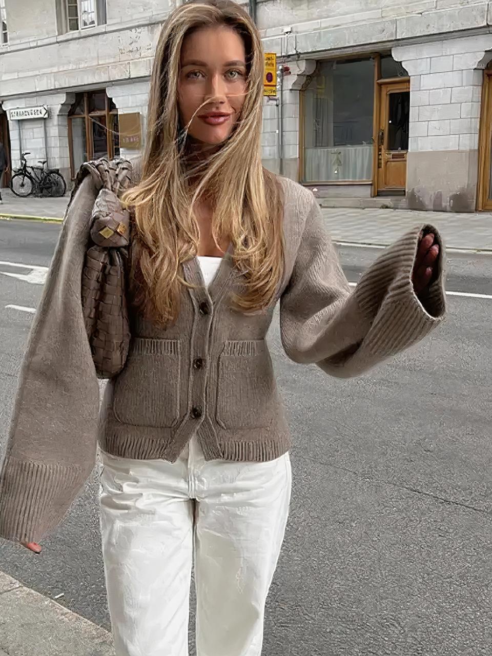 Femme portant un gilet cardigan beige et un pantalon blanc.