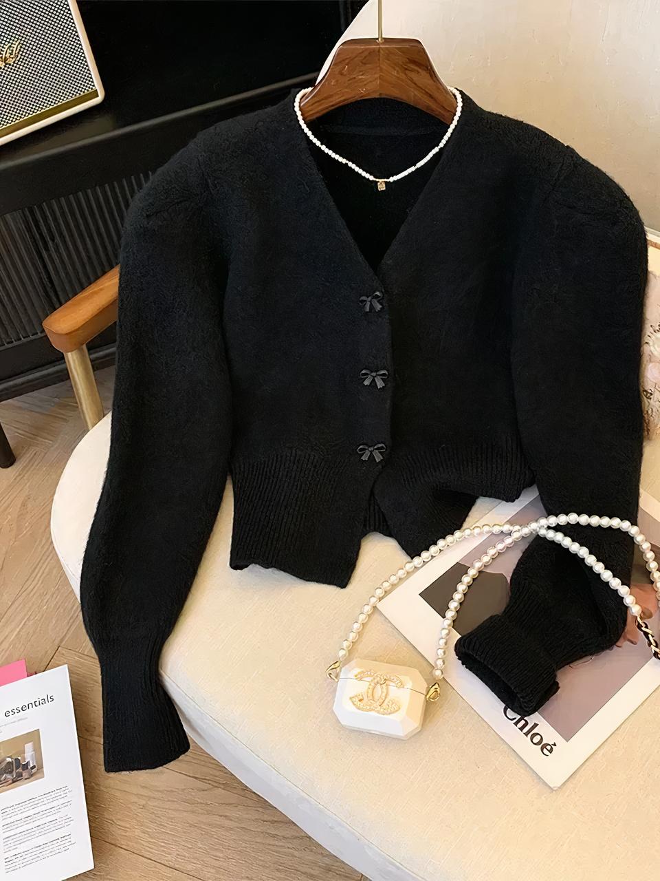 Gilet cardigan noir sur un cintre et posé sur un fauteuil.