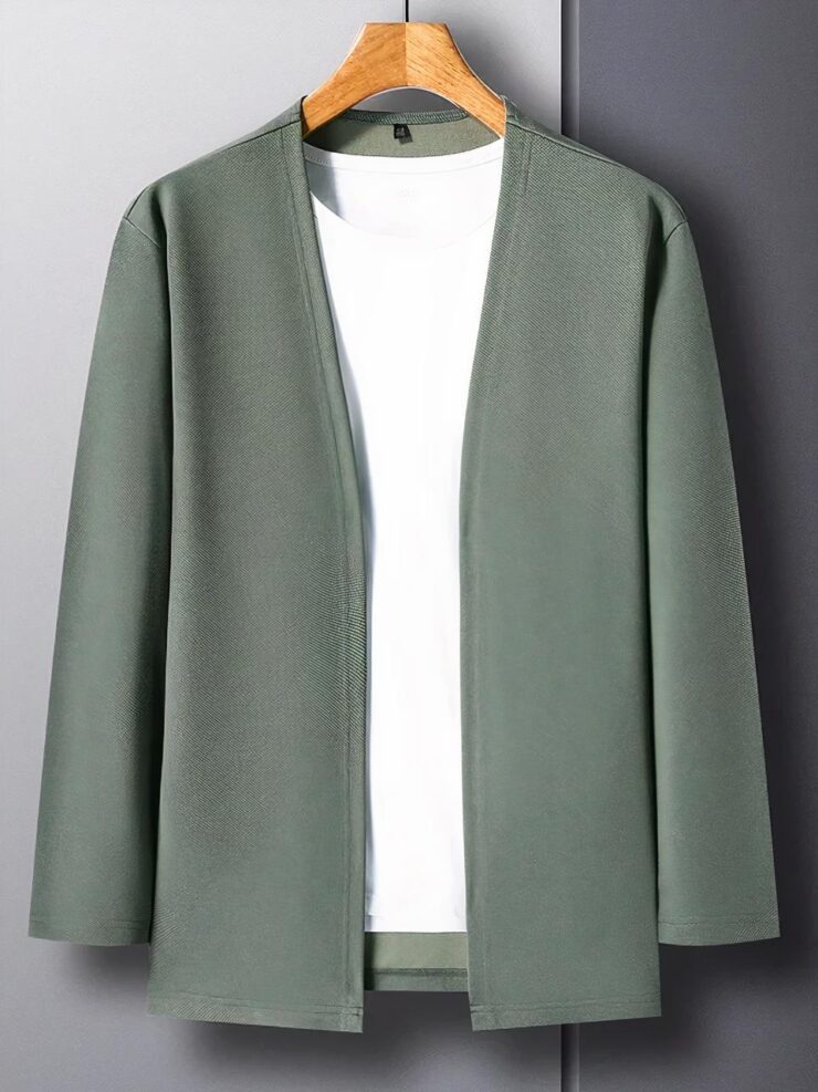Photo d'une veste cardigan verte pour homme au design très simple sans col, encolure en V et manches longues sur un top blanc le tout sur un cintre en bois clair, photo prise sur un fond gris clair à gauche et gris foncé à droite