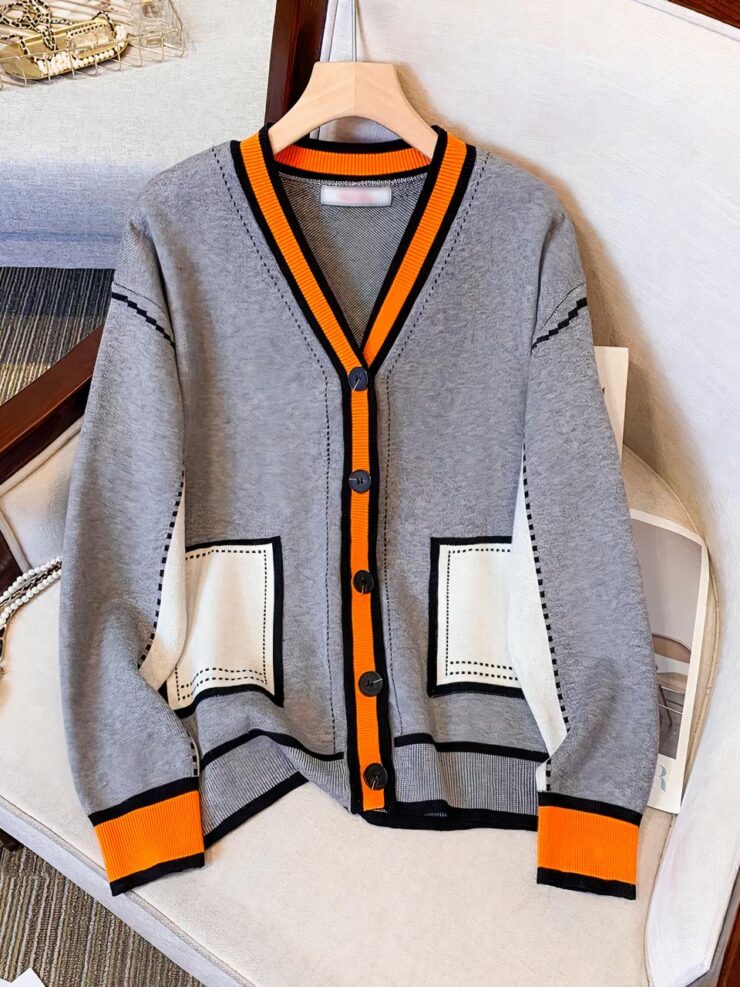 Un gilet gris avec des poches blanches, des poignets, la boutonnière et le contour du col orange est posé sur un fauteuil blanc