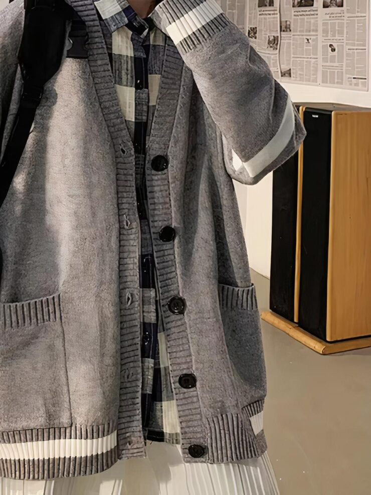 Un homme porte un pantalon beige, une chemise à carreaux noirs et blancs et un gilet large gris avec des bandes blanches aux coudes, aux poignets et en bas