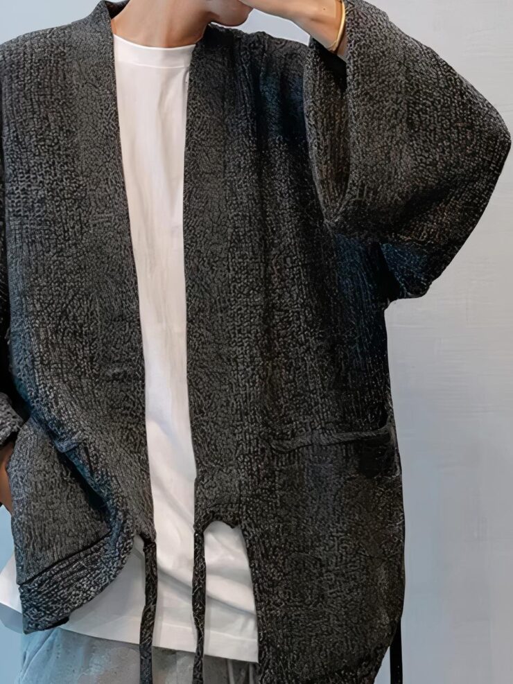 Un homme porte un jean, un tee shirt blanc et une veste grise large avec des poches et deux cordons pendants